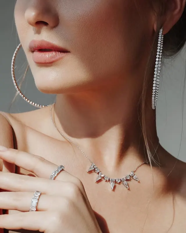 A model wearing a diamond necklace, diamond hoop earrings and two diamond rings.