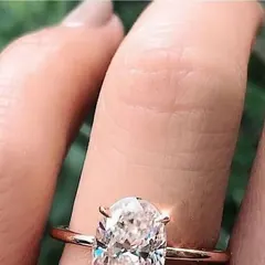 An oval solitaire engagement ring held between two fingers.